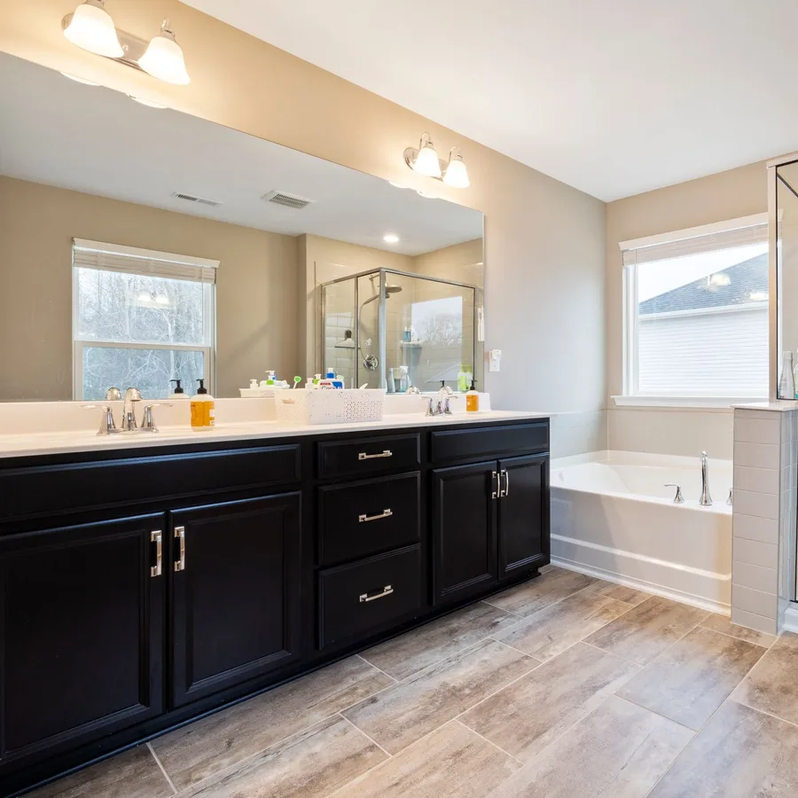Bathroom remodel with a black double vanity, wood-look tile floor and glass shower