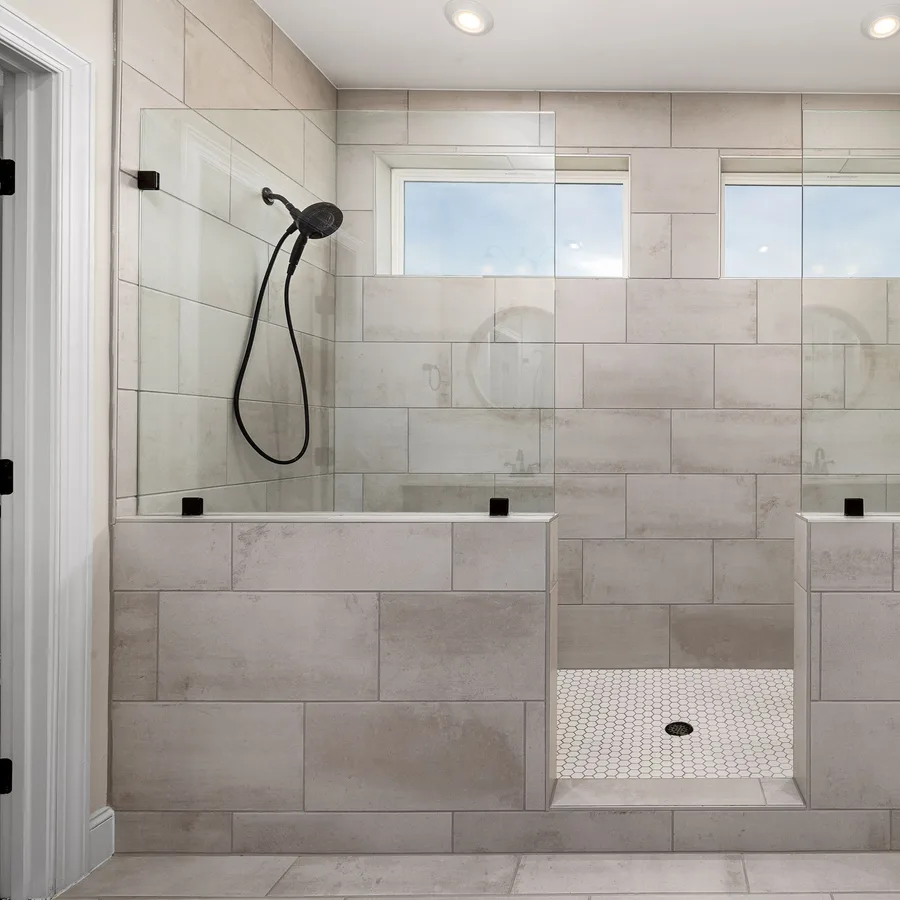 Remodeled walk-in shower with gray porcelain tile, a half wall and two shower heads